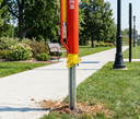 Red and yellow utility pole on a sidewalk with trees and a bench in the background